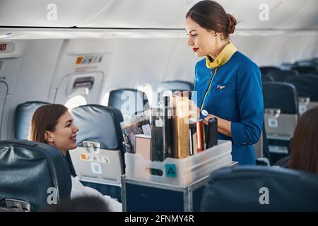 Frau im Flugzeug, die den Flugbegleiter mit einem Essenswagen ansprach Stockfoto