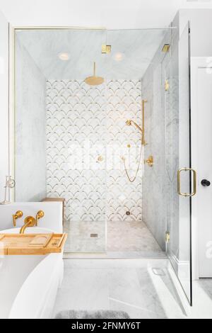 Eine wunderschöne geflieste Dusche und Badewanne mit Gold- und weißen Fliesen an den Wänden, Mosaikmarmorfliesen auf dem Boden und einem goldenen Duschkopf und Hardware. Stockfoto