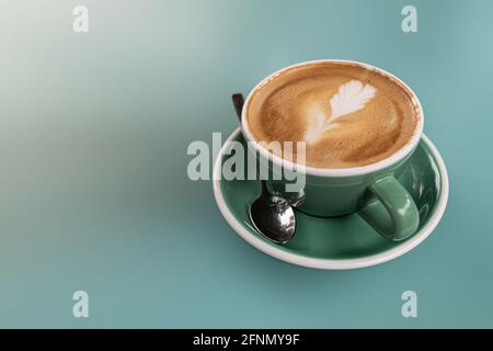 Ein heißer Latte in einem grünen Keramikbecher auf einem Ton in Ton blau türkisfarbener Hintergrund Stockfoto