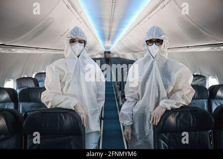 Zwei Mitarbeiter der Kabinencrew in Schutzüberalls in der Flugzeugkabine Stockfoto