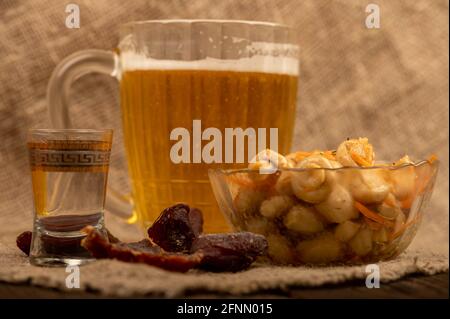 Eingelegte Pilze in einer Glasplatte, ein Glas Wodka und ein Becher Bier auf einem Tisch, der mit einem weichen Tuch bedeckt ist. Nahaufnahme, Selecti Stockfoto