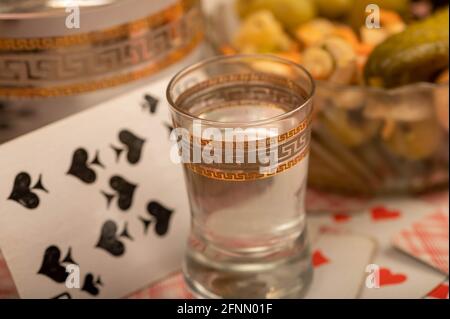 Spielkarten, ein Glas Wodka, ein Dekanter Wodka und eine Glasschale mit Gurken und Pilzen auf dem Tisch. Nahaufnahme, selektiver Fokus. Stockfoto