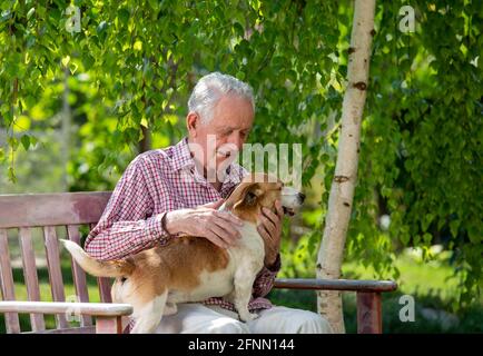 Älterer Mann sitzt im Garten mit niedlichem Hund im Schoß Und kuscheln Stockfoto
