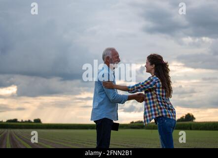 Ältere Bäuerin und junge Frau schütteln sich die Hände auf dem Feld Stockfoto