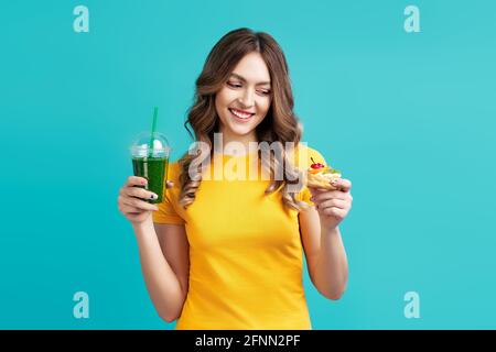 Glückliche Frau wählen ungesunde Kuchen mit Smoothie Detox Saft auf blauem Hintergrund. Essen, Diät-Konzept. Stockfoto