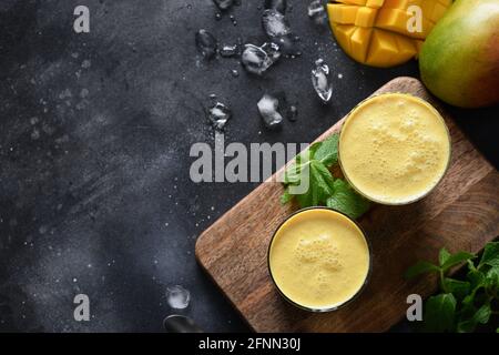 Zwei Mango Lassi oder Smoothies auf schwarzem Hintergrund, Draufsicht mit Kopierraum. Indische traditionelle kalte Mangolassi aus Joghurt, Wasser, Gewürzen, Früchten Stockfoto