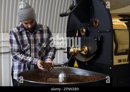 Mann mit gerösteten Kaffeebohnen, Mann mit der Hand mit Kaffeebohnen aus dem Röster Stockfoto