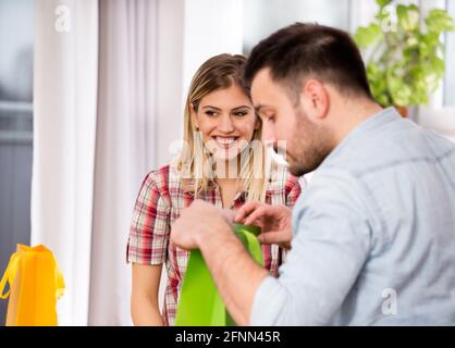 Glückliches junges Paar, das Geschenke in Einkaufstaschen auf dem Sofa wechselt Zu Hause Stockfoto