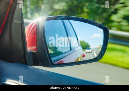 Spiegelung eines verschwommenen Autos im Rückspiegel auf der Autobahn An einem schönen sonnigen Tag Stockfoto