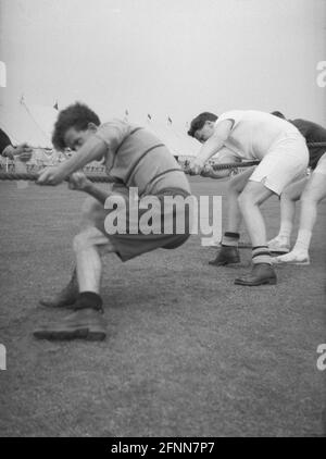 1954, historisch, draußen auf einem Feld, an einem Sporttag des öffentlichen Dienstes, ziehen männliche Konkurrenten hart am Seil in einem Tauziehen-Wettbewerb, England, Großbritannien. Interessante Schuhe, die Front zwei Männer tragen schwere Stiefel, möglicherweise Ex-Armee, während auf der Rückseite der Mann Pilmsols trägt. Ein alter Sport, und Teil der Olympischen Sommerspiele von 1900-1920, ist das Tauziehen ein Test der Stärke zwischen zwei Teams mit dem Ziel, das Seil eine gewisse Distanz in eine Richtung gegen die Kraft des Zuges des gegnerischen Teams zu bringen. Stockfoto