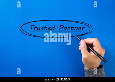Geschäftsmann Hand schreiben ein Trusted Partner Zeichen mit schwarzem Marker auf blauem Hintergrund. Stockfoto