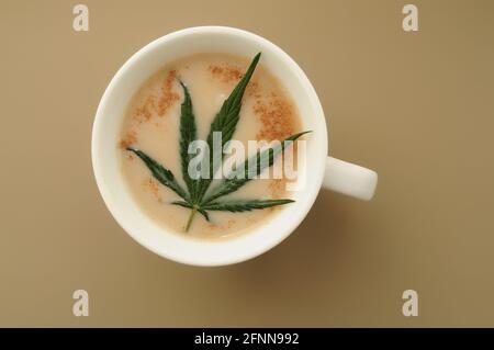 Marihuana Cappuccino mit Zimt. Tasse Bio-CBD-Kaffee. Cannabisküche. Heißes Getränk isoliert auf braunem Hintergrund, flach liegend, Draufsicht. Stockfoto