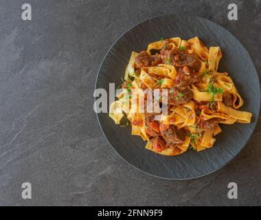 Pasta mit italienischem Rindereintopf auf einem dunklen Teller Auf dunklem Tischhintergrund mit Kopierfläche Stockfoto