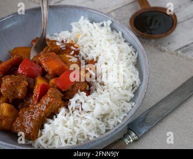 Würziger philippinischer Schweinestew afritada serviert mit Basmati-Reis Eine rustikale Schüssel auf einem Holztisch Stockfoto