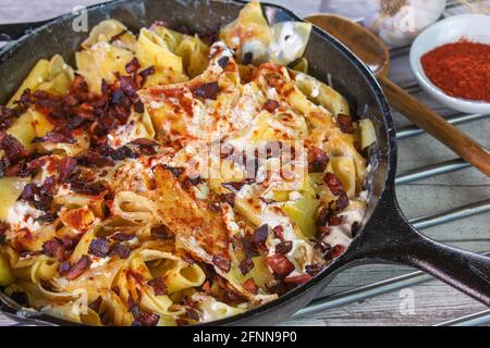 Rustikales ungarisches Nudelgericht Turos csusza mit Quark, Quark und Speck, serviert in einer gusseisernen Pfanne auf einem Tisch Stockfoto