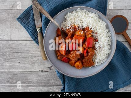 Würziger Schweinestew afritada serviert mit Basmati-Reis in einem Rustikale Schüssel auf Holztisch Hintergrund Stockfoto