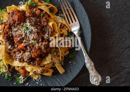 Frisch und hausgemacht gekochte Linsen Bolognese mit Pasta serviert auf dunklem Teller mit rustikaler Gabel auf dunklem Tischhintergrund mit Kopierplatz, Stockfoto