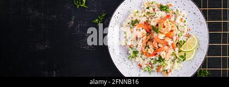 Couscous mit gerösteten Garnelen, Tomaten, roten Zwiebeln, Mandelnüssen und Petersilie. Marokkanisches Essen mit Couscous und Garnelen. Draufsicht, Banner Stockfoto