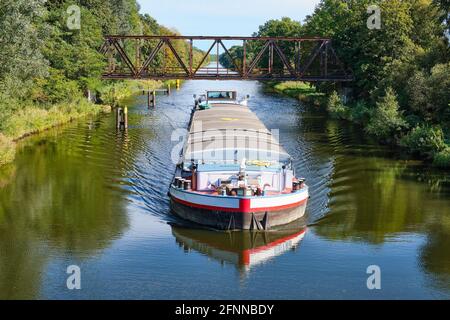 Das Frachtschiff passiert an einem sonnigen Herbsttag unter einer alten Eisenbrücke. Reflexionen im Wasser Stockfoto