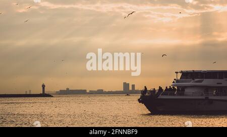 Silhouette einer Yacht auf dem ruhigen Wasser mit dem Stadt im Hintergrund Stockfoto
