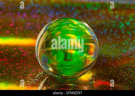 Glaskugel mit humanoidem Gesicht innen auf abstraktem holographischem Hintergrund aus nächster Nähe. Futuristische Retro-Collage. Stockfoto