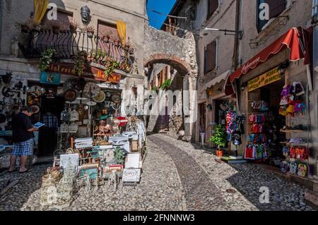 Eine schmale gepflasterte Straße mit Touristenläden unter der Straße Ein mittelalterlicher Torbogen in der mittelalterlichen Stadt Malcesine On Das Ostufer des Gardasees i Stockfoto