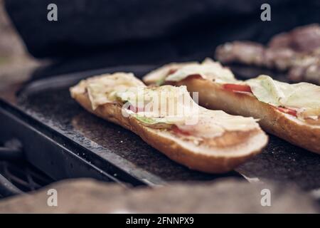 Gegrilltes Baguette, mit Butter und Öl, Hühnerschinken, Tomaten verschmiert und mit Käse überzogen, wird auf einem Granitstein goldbraun gebacken Stockfoto