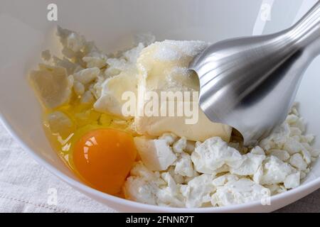 Quark, Butter, Ei und Zucker in einer weißen Schüssel – Zutaten zum Mischen mit einem Stabmixer. Der Prozess der Herstellung von Quark Bagels oder Croissants Stockfoto