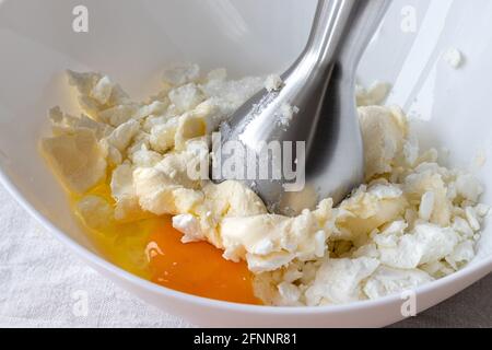 Quark, Butter, Ei und Zucker in einer weißen Schüssel – Zutaten zum Mischen mit einem Stabmixer. Der Prozess der Herstellung von Quark Bagels oder Croissants Stockfoto