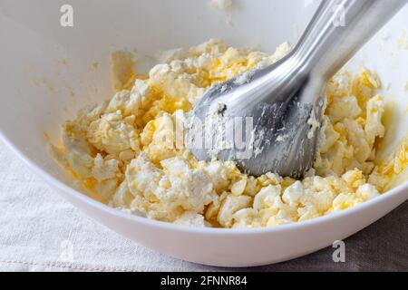 Teig in einer weißen Schüssel mit einem Stabmixer mischen. Zutaten - Quark, Butter, Ei und Zucker. Der Prozess der Herstellung von Quark Bagels oder Crois Stockfoto