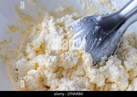 Teig in einer weißen Schüssel mit einem Stabmixer mischen. Zutaten - Quark, Butter, Ei und Zucker. Der Prozess der Herstellung von Quark Bagels oder Crois Stockfoto