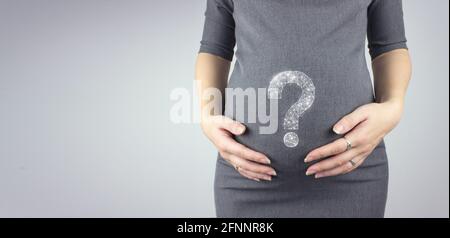 Junge Frau, die den schwanger Bauch in den Händen mit einem Hologramm-Fragezeichen hält. Schwangerschaft, Mutterschaftskonzept. Stockfoto