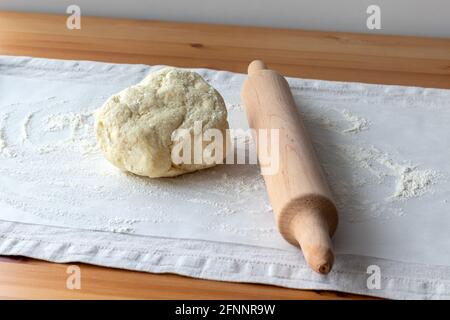 Roher Quark-Teig mit Stückchen Quark, hölzernen Nudelholz und bestreut Mehl auf Backpapier auf einem Leinentischtuch auf einem Holztisch Stockfoto