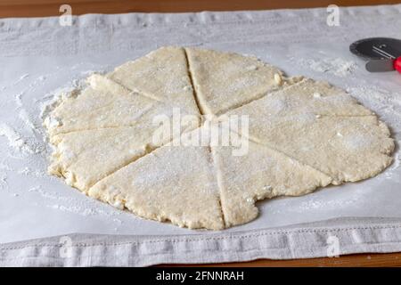 Gerollter roher Quark-Teig mit Stücken Quark geschnitten In acht Dreiecke mit Zucker auf Backpapier bestreut Eine Leinentischdecke auf einem Holztisch Stockfoto