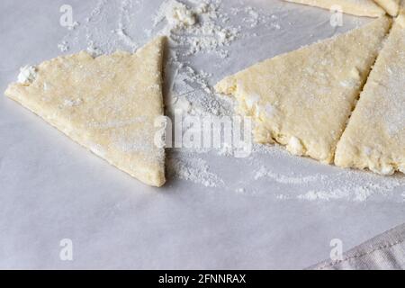 Gerollter roher Quark, der in acht mit Zucker bestreute Dreiecke geschnitten wird, und ein Teigdreieck liegt getrennt auf Backpapier auf einer Leinentischdecke. T Stockfoto