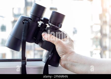 Hand hält ein schwarzes Fernglas vor einem verschwommenen Hintergrund Stockfoto