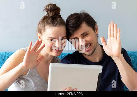 Ein lächelndes Ehepaar begrüßt Eltern oder Freunde bei einem Online-Anruf über ein Tablet. Ein Mann und eine Frau, eine zweiköpfige Familie, tätigen während eines Streites einen Videoanruf Stockfoto