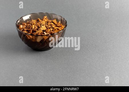 Bio hausgemachte geröstete Müslis mit Hafer, Flachs, Mandeln, Schokolade in runder Glasschale auf grauem Hintergrund mit Kopierfläche. Natürliches Müsli Stockfoto