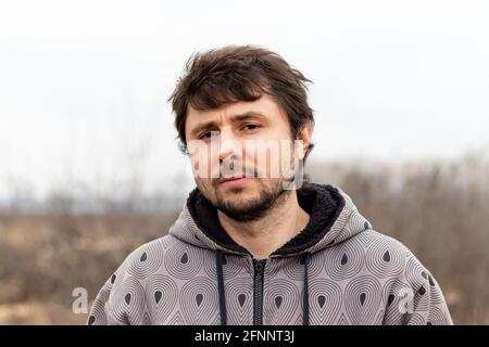 Ein hübscher bärtiger Mann mit zerzaust geschräunten Haaren vor einem verschwommenen Hintergrund. Mann in einer Jacke mit Kapuze Stockfoto