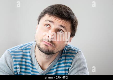 Nachdenklicher, hübscher bärtiger Mann in einem gestreiften Pullover, der nach oben schaut Stockfoto