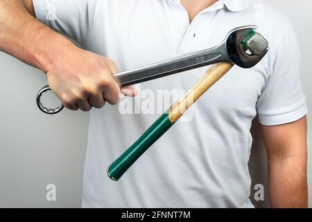 Ein Mann in einem weißen T-Shirt hält einen Schraubenschlüssel fest Mit einem Hammer daran hängen Stockfoto