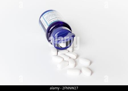 Weiße Glucosaminsulfat-Tabletten, die aus einem offenen Blau auslaufen Kunststoffbehälter auf weißem Hintergrund Stockfoto