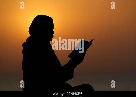 Silhouette einer muslimischen Frau, die bei Sonnenuntergang den Edlen Koran liest. Religion beten Konzept. Vereinigte Arabische Emirate Stockfoto