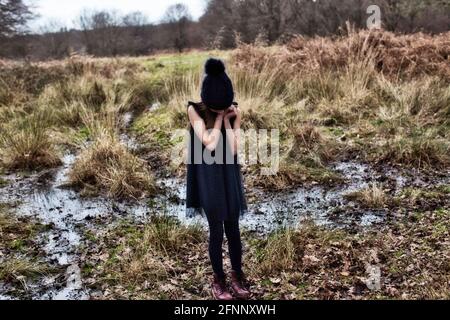 Ein kleines Mädchen, das in einer unheimlichen, gruseligen Landschaft steht. Mädchen, das auf einem Moor steht Stockfoto