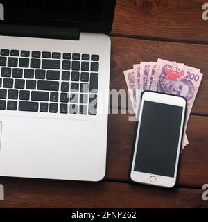 Laptop, Telefon und Geld auf Holzhintergrund. Technik und ukrainisches Geld Stockfoto