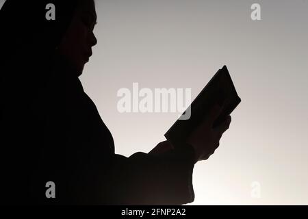 Silhouette einer muslimischen Frau, die den Edlen Koran gegen den Himmel liest. Religion beten Konzept. Vereinigte Arabische Emirate Stockfoto