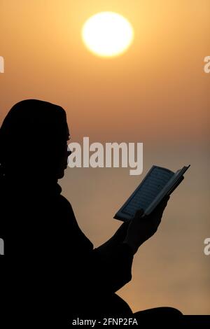 Silhouette einer muslimischen Frau, die bei Sonnenuntergang den Edlen Koran liest. Religion beten Konzept. Vereinigte Arabische Emirate Stockfoto