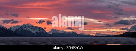 Atemberaubender Sonnenuntergang über schneebedeckten Berggipfeln im Norden Kanadas im Frühling mit violetten, pfirsichfarbenen und rosafarbenen Farben und eisigem See. Stockfoto