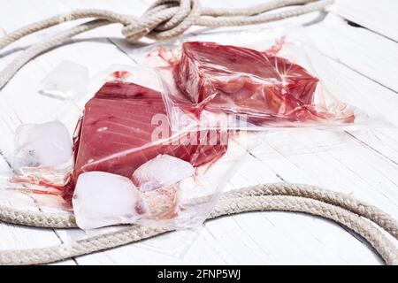 Rote Thunfischfilets in Vakuumverpackung auf weißem Holzhintergrund. Frischer Fisch, Zitrone und Petersilie zum Kochen von Zutaten. Konzept der gesunden Ernährung. Prot Stockfoto