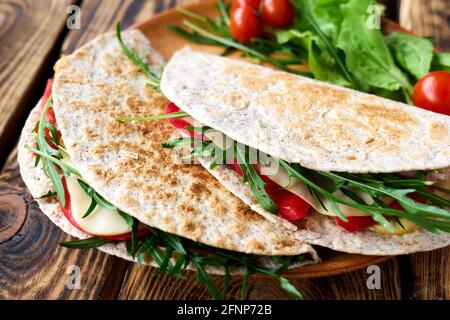 Piadina Romagnola mit Mozzarella-Käse, Tomaten, Schinken und Rucola-Salat auf Holztisch. Italienisches Fladenbrot oder offenes Sandwich. Selektiver Fokus. Stockfoto